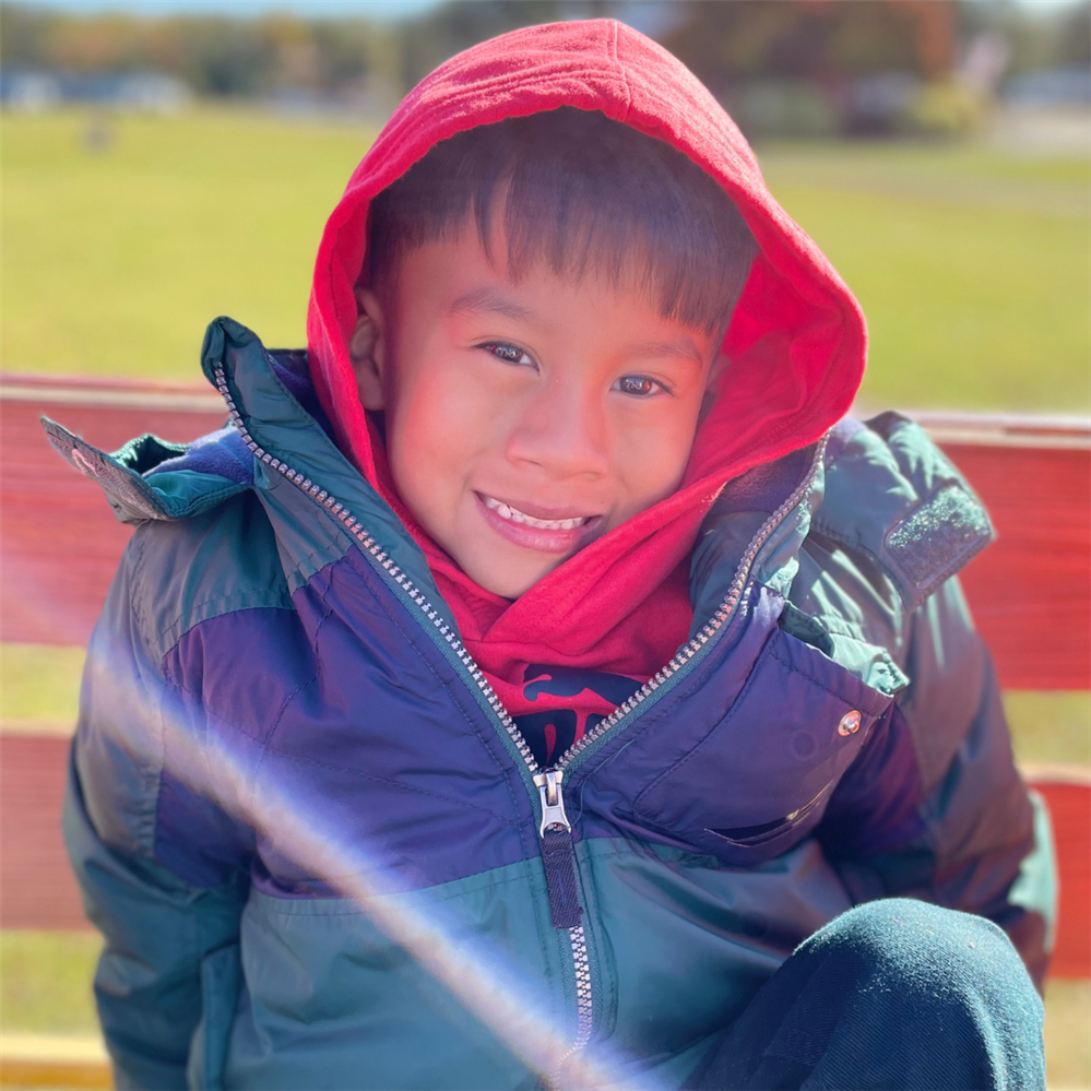 a young boy in a red jacket smiles at the camera TEXT: 2023-24 new student and kindergarten registration
